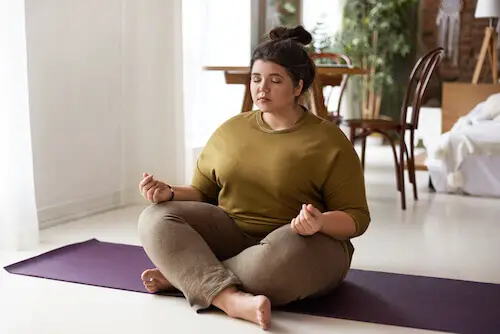 harmony balance zen peace concept indoor shot plus size barefoot young brunette woman with hair bun sitting mat keeping legs crossed eyes shut meditating after yoga practice 1 1